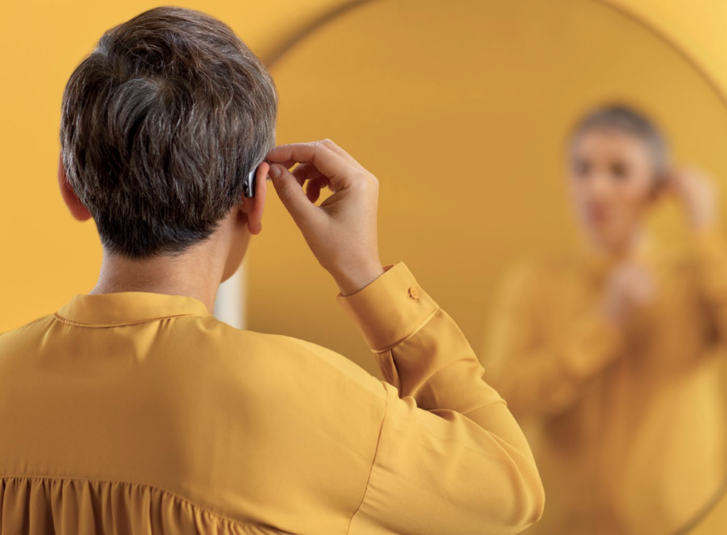 Woman adjusting hearing aid in ear.